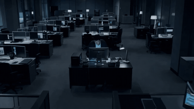 Gen-4_5 A cranejib shot moves smoothly downwards, revealing a lone figure hunched over a desk in a dimly lit office, the camera stopping to frame their face as they stare intently at a glowing monitor.mp4.gif
