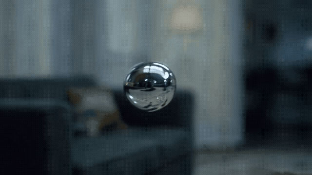 Gen-4_5 A shallow focus shot isolates a single, chrome ferrofluid bubble floating impossibly slowly across a dimly lit, silent room, its warping surface reflecting a distorted, blurred reality, while .mp4.gif